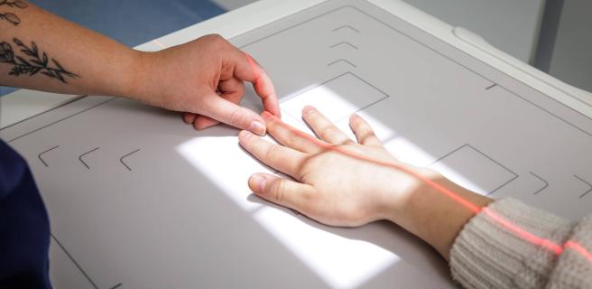 En hand placerar den andra handen på röntgenapparaten.