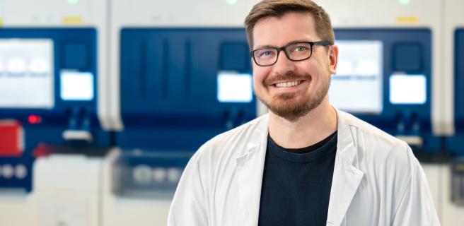 HUSin lääkäri valkoisessa takissa seisoo laboratorion analyysilaitteiden edessä.