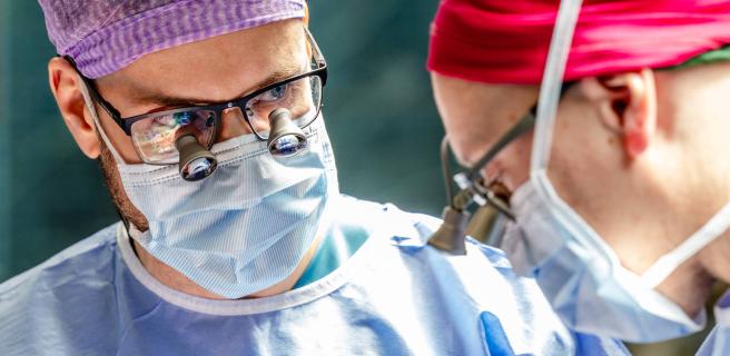 Kaksi leikkaussalissa työskentelevää lääkäriä leikkausasuissa ja -maskeissa.