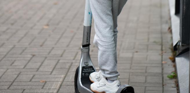 Henkilö ajaa potkulaudalla harmaissa housuissa ja valkoisissa lenkkareissa.
