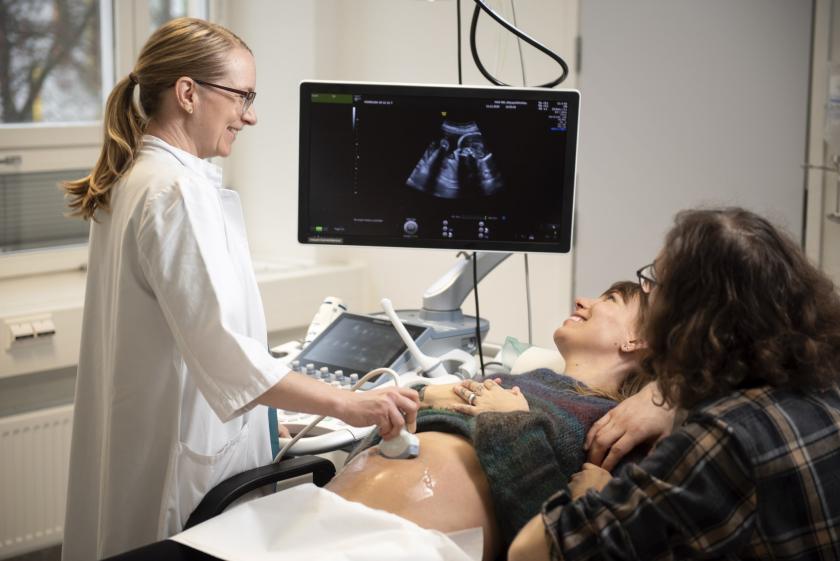 Kuvituskuva: Lääkäri tekee raskaana olevalle naiselle ultraäänitutkimuksen, tukihenkilö seuraa vieressä