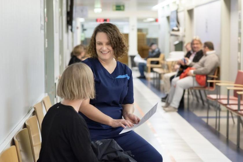 Sairaanhoitaja juttelee potilaalle käytävällä.