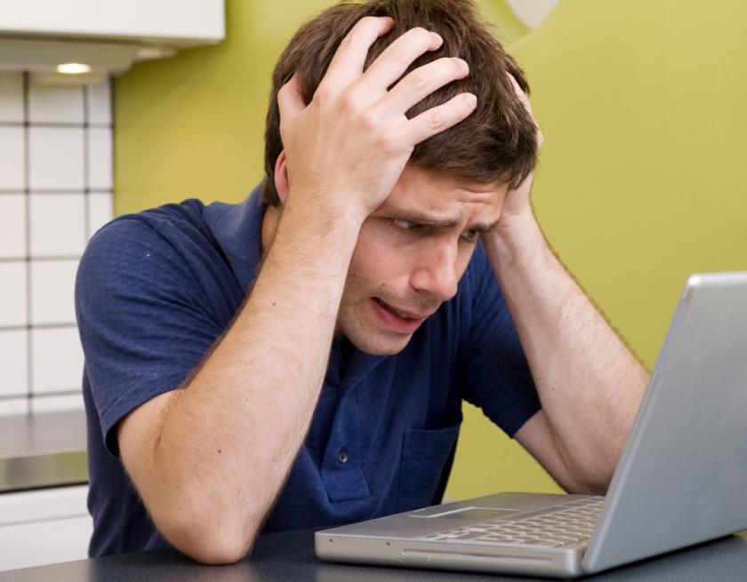 Mies pitelee käsillään päätä kannettavan tietokoneen edessä ja näyttää tuskaiselta.