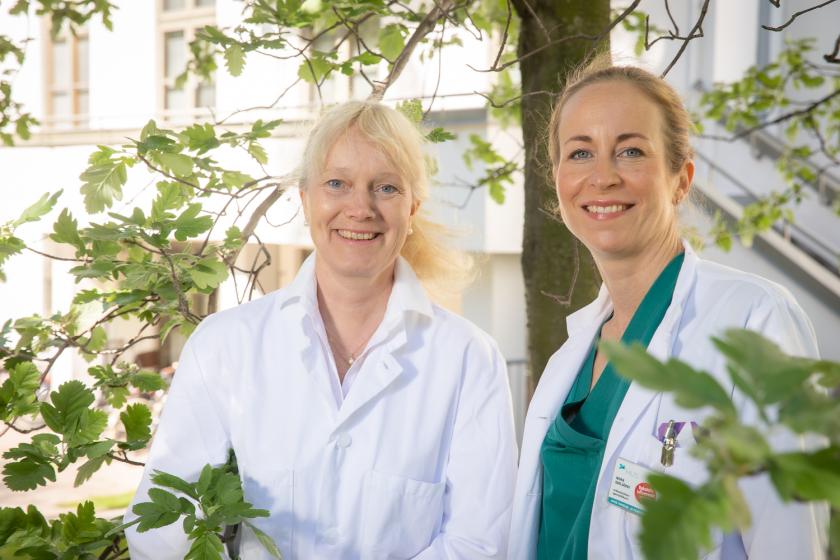 Kaksi naista lääkärintakeissa vihreän puun alla.