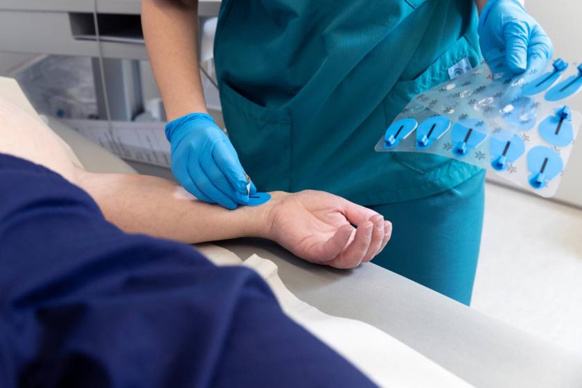 Hoitajan käsi kiinnittää elektrodia potilaan käteen.