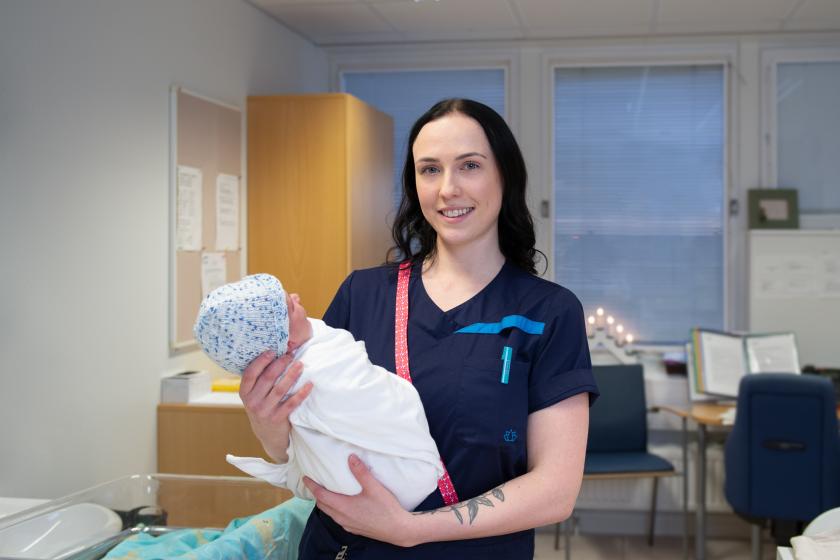 Lähihoitaja Christa Ekfors katsoo kameraan ja pitelee sylissään vauvaa.