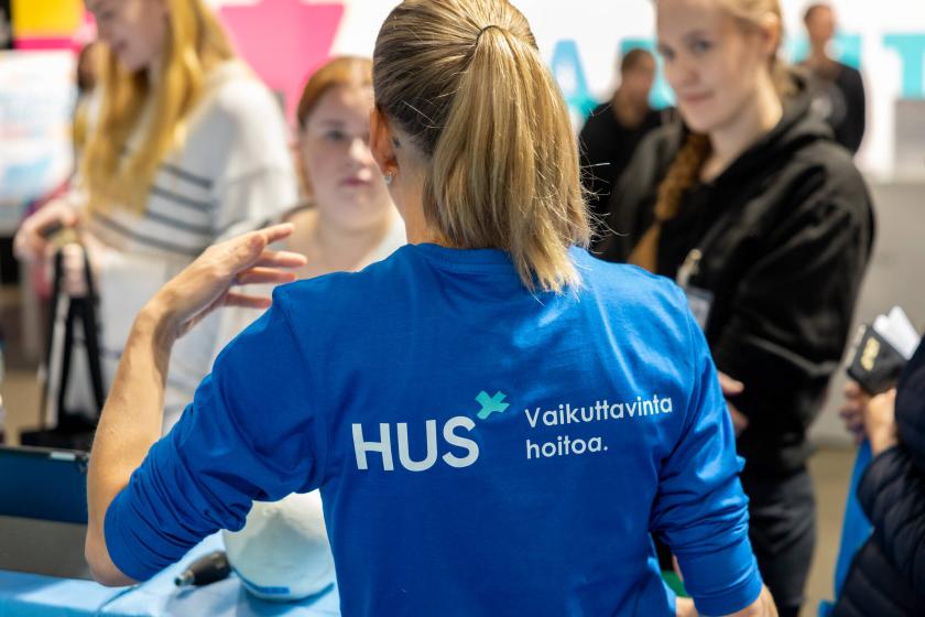 Nainen messuilla kertoo kahdelle kuulijalle HUSin toiminnasta
