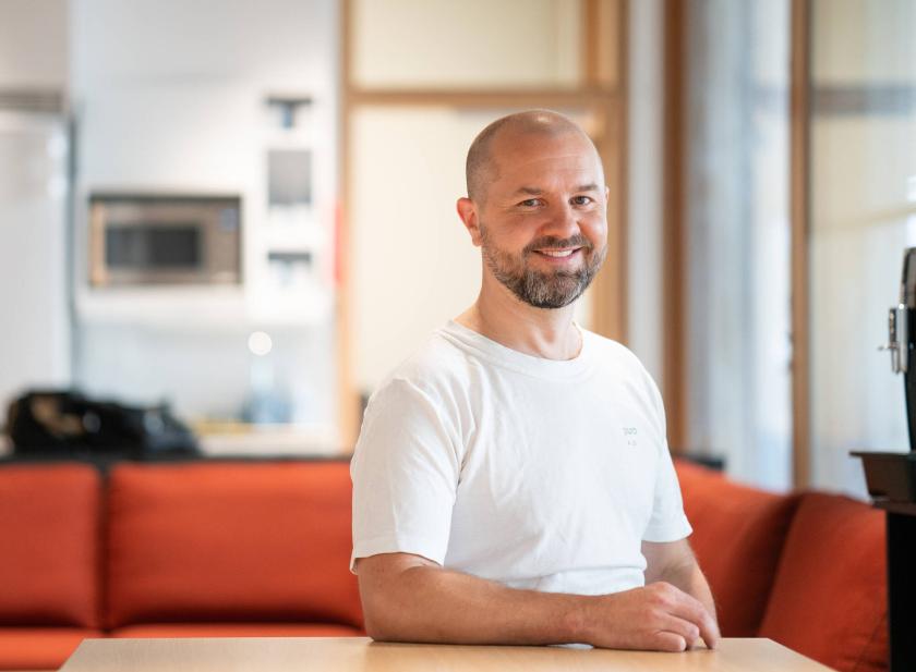 Mies valkoisessa paidassa oranssilla sohvalla pöydän ääressä.