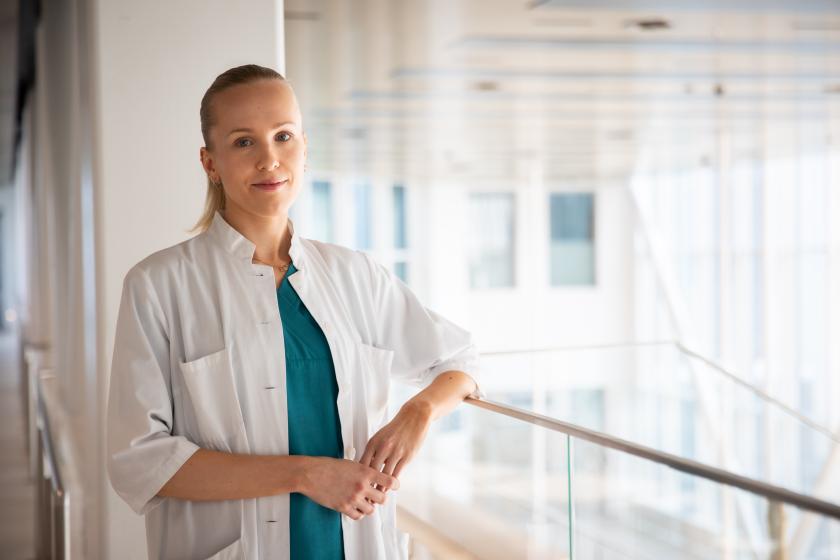 Henkilö valkoisessa takissa seisoo käytävällä ja hymyilee.