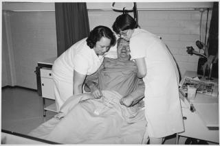 Apuhoitajia nostamassa potilasta Joutsan terveyskeskuksen vuodeosastolla vuonna 1983. Kuva: Liisa Kiiski, SuPer.