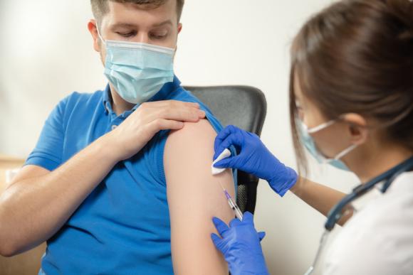 Hoitaja laittaa miehelle rokotuksen käsivarteen.