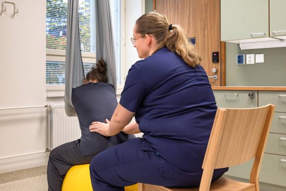 Kätilö tukee jumppapallon päällä istuvaa naista synnytyksessä