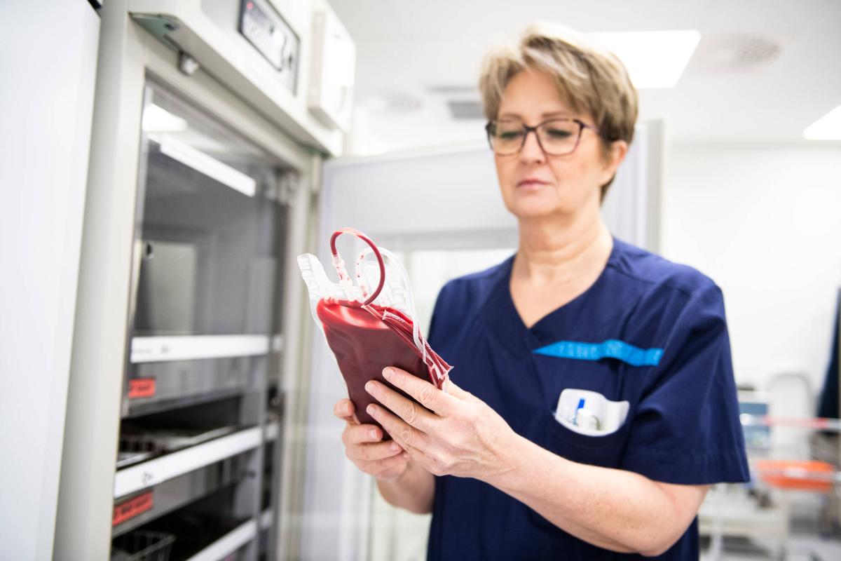 En laboratorieskötare håller en blodpåse framför kylskåpet.