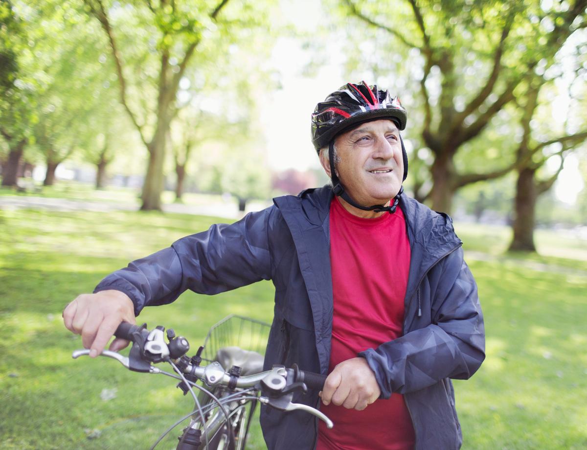 En äldre person som antas vara en man med sin cykel i en somrig park.