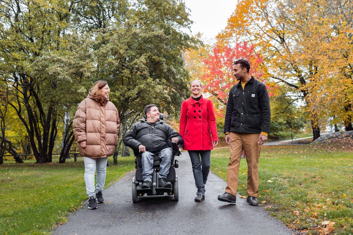 Tre vuxna och en vuxen i rullstol i en park.