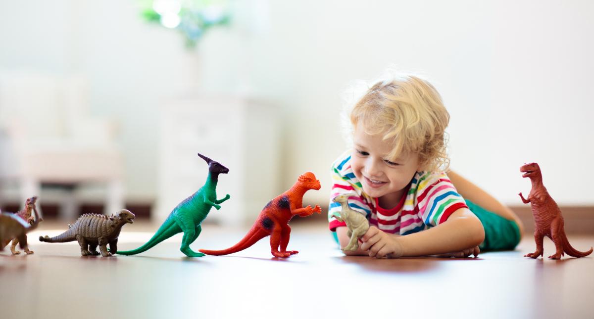 Lapsi leikkii lattialla maaten dinosauruksilla.