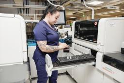 A laboratory nurse placing sample tubes in to a machine.