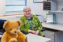 HUSin työterveyshoitaja Tarja Siik istuu työpöydän ääressä pehmonalle kuvan etualalla.