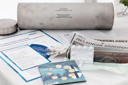 metallilieriön edessä sanomalehtiä, tilaisuuden ohjelma, lääketarvikkeita ja kolikoita