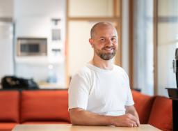 Mies valkoisessa paidassa oranssilla sohvalla pöydän ääressä.