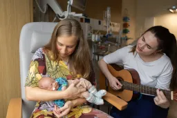 Äiti pitää sylissään keskosvauvaa ja musiikkiterapeutti soittaa kitaraa vieressä.
