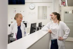 Lääkäri ja musiikkiterapeutti keskustelevat osaston infotiskin äärellä.