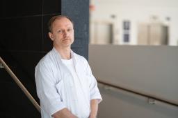 En man i vit skjorta står vid en vägg i en modern byggnadsinteriör.